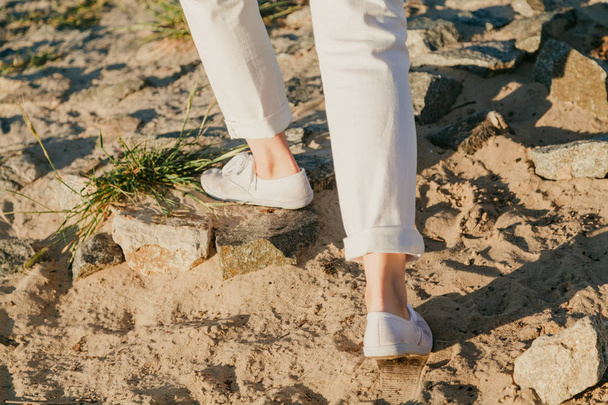 Legs of  woman in white shoes walking on sand - Photo, image