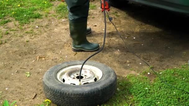 Un hombre infla una rueda vieja del coche con un compresor
. - Metraje, vídeo