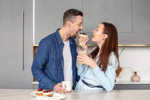 Feliz joven pareja bebiendo té con dulces en casa
 - Foto, Imagen