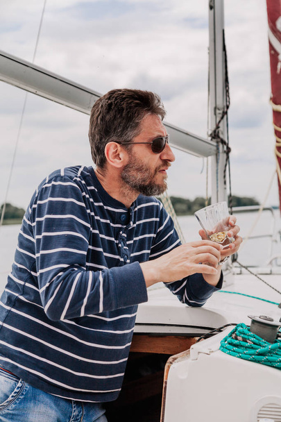 Man with beard in glasses drinks whiskey on yacht - Photo, Image