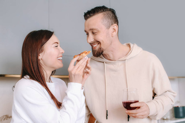 Ευτυχισμένο ζευγάρι πίνοντας κρασί και τρώγοντας νόστιμη πίτσα στο σπίτι - Φωτογραφία, εικόνα