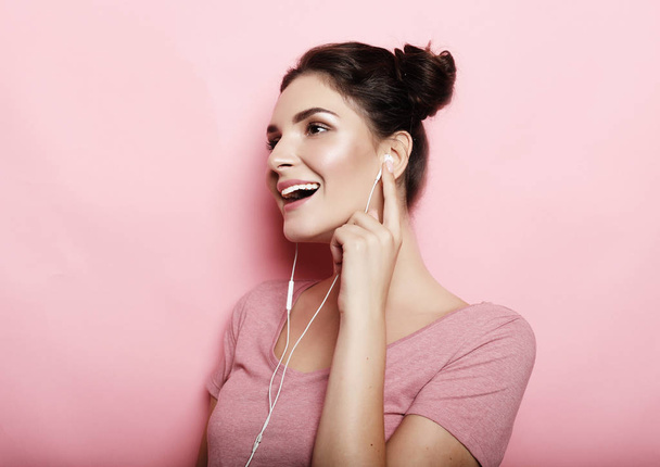 Beautiful young woman in headphones listening to music over pink background - Foto, Bild