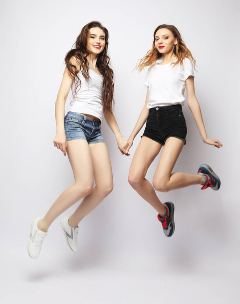 Two happy carefree young women jumping over white background - Fotó, kép