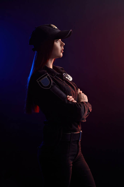 Serious female police officer is posing for the camera against a black background with red and blue backlighting. - Fotografie, Obrázek