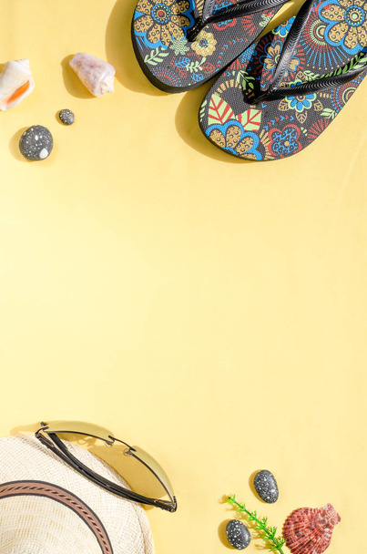 Vakantie en zomer vakantie concept. Platte lay van stro hoed, zonnebril, flip flops en schelpen op gele achtergrond - Foto, afbeelding