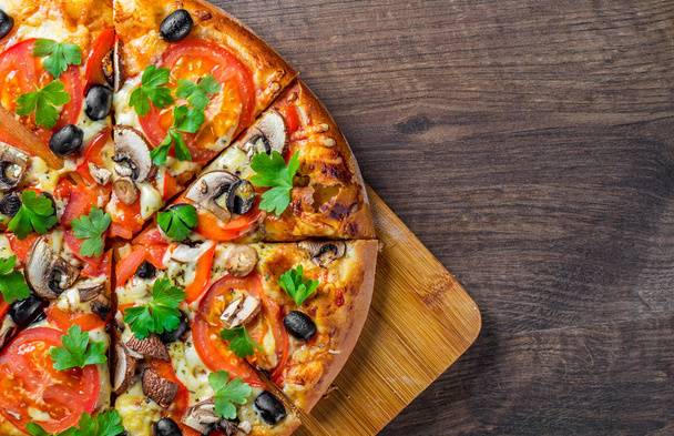 sliced Pizza with Mozzarella cheese, Tomatoes, pepper, olive, mushrooms, Spices and Fresh leaf. Italian pizza on wooden table background - Fotó, kép