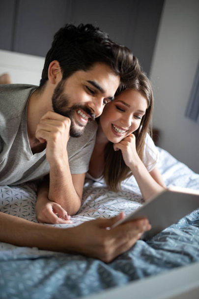 Cheerful couple looking a tablet together and laughing while lying on the bed - Fotó, kép