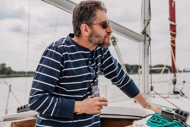 Man with beard in glasses drinks whiskey on yacht - Фото, зображення