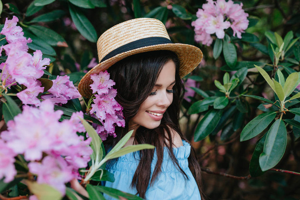 Portrait of young beautiful woman in straw hat posing among blooming trees - Фото, изображение