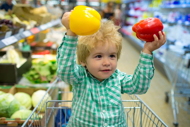 Child and vegetables. Healthy food. The boy holds red and yellow peppers in his hands. Supermarket. - Photo, Image