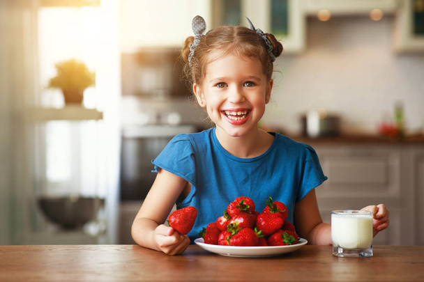 ミルクでイチゴを食べる幸せな子供の女の子   - 写真・画像