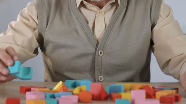 Old man with Alzheimers disease trying to concentrate on task with colored cubes - Кадры, видео