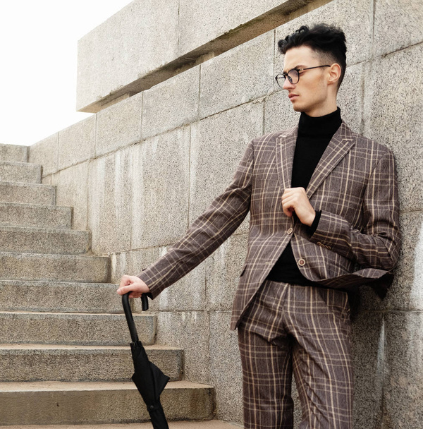 fashionable young man in glasses with umbrella standing on the stairs - 写真・画像