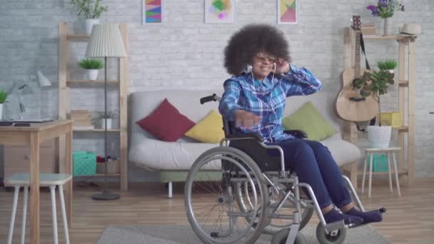 cheerful disabled african american woman with an afro hairstyle in a wheelchair in headphones listening to music - Metraje, vídeo