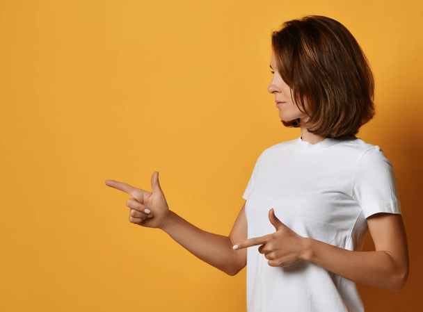 Woman in white t-shirt and blue jeans point finger shows finger-gun sign at free text space - Fotoğraf, Görsel