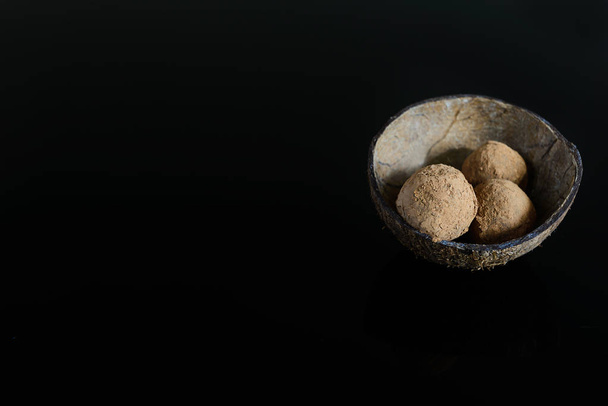 Energy balls of date fruits, nuts and cocoa on a dark background. Raw dessert in a coconut shell, with a copy space. - Foto, afbeelding