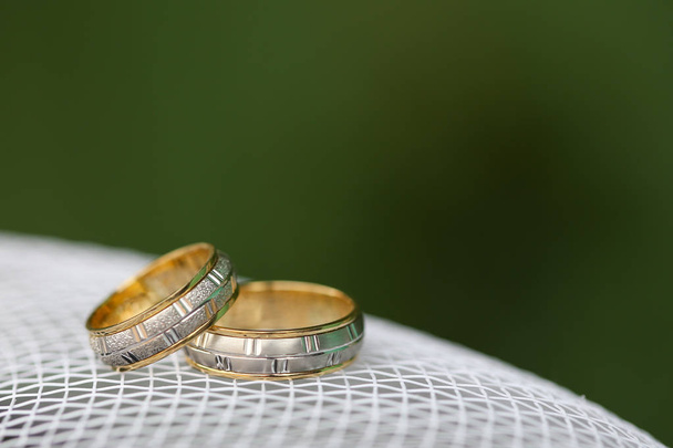 Χρυσά δαχτυλίδια γάμου στο λευκό πλέγμα με πράσινο φόντο - Φωτογραφία, εικόνα