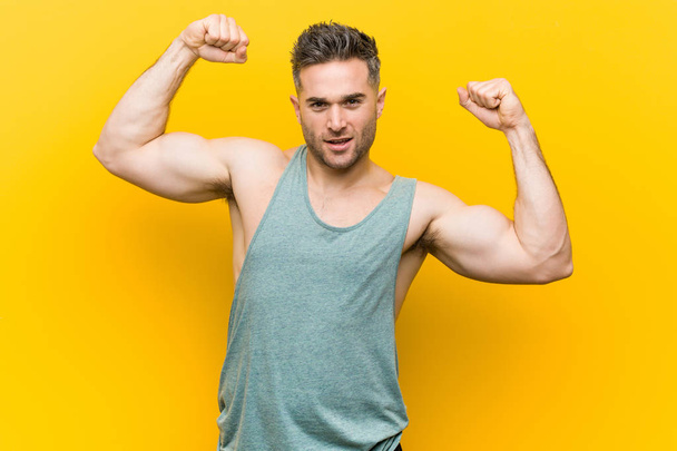 Fiatal fitness férfi sárga háttér mutatja erő gesztus karokkal, szimbóluma a női hatalom - Fotó, kép