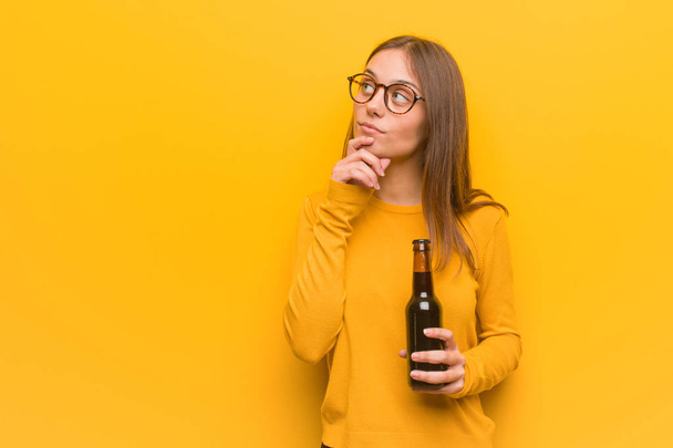 Young pretty caucasian woman doubting and confused. She is holding a beer. - Photo, Image