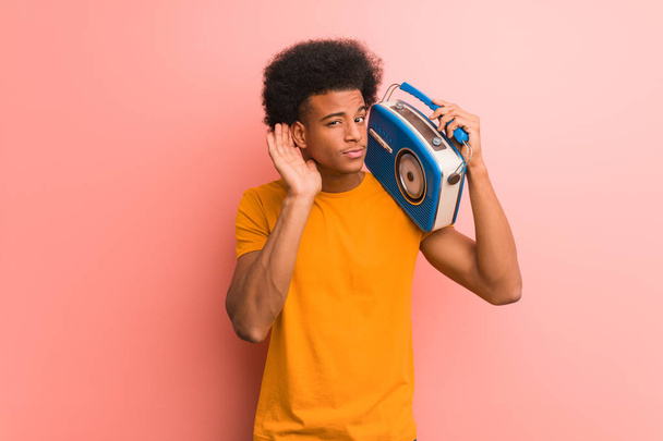 Jeune afro-américain tenant une radio vintage essayer d'écouter un potins
 - Photo, image