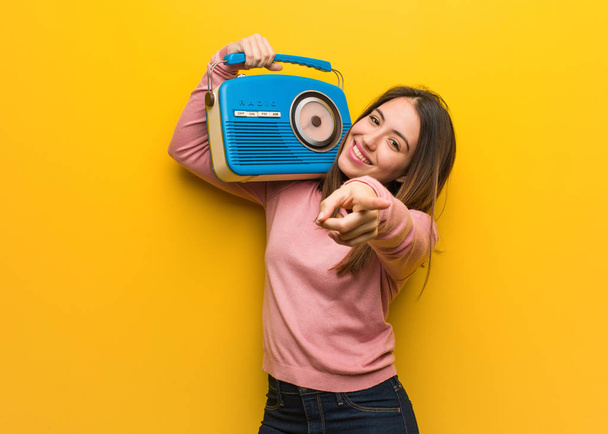 junge süße Frau hält ein Vintage-Radio fröhlich und lächelnd nach vorne zeigend - Foto, Bild