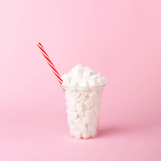 Plastic cup with straw full of sugar cubes on pink background Unhealthy drink concept - Foto, Imagen