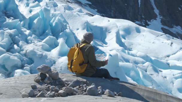 Vousatý muž se žlutým batohu a turistická mapa v rukou, na pozadí zimní krajiny - Záběry, video