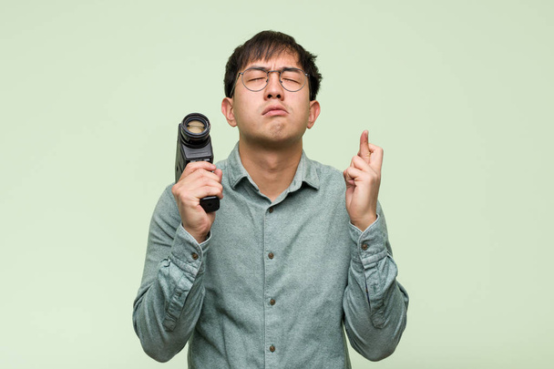Fiatal kínai férfi kezében egy vintage kamera keresztbe ujjait, mert a szerencse - Fotó, kép