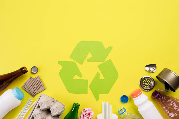 Top view of Different garbage materials with recycling symbol on yellow background. Recycle, World Environment Day and Eco concept - Photo, Image