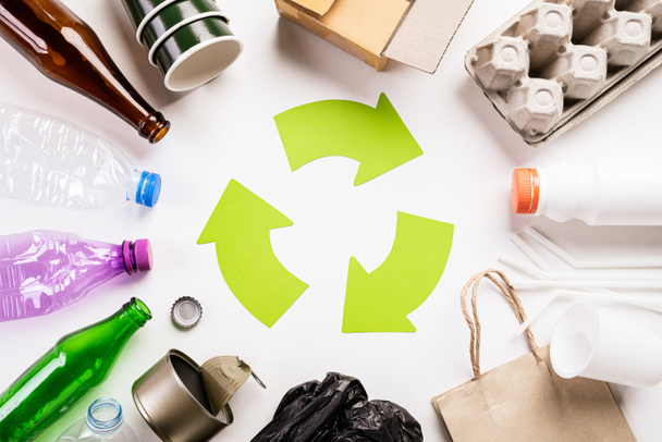 Vista superior de diferentes materiales de basura con símbolo de reciclaje sobre fondo de mesa de madera blanca. Reciclaje, Día Mundial del Medio Ambiente y concepto ecológico
 - Foto, imagen