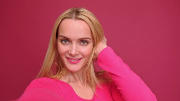 Attractive young woman blonde in a red T-shirt and jeans posing on a pink background. - Кадри, відео