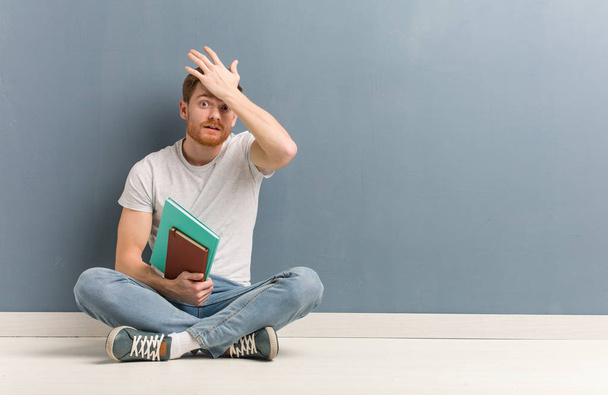 Молодой рыжий студент, сидящий на полу взволнованный и потрясенный. Он держит книги.
. - Фото, изображение