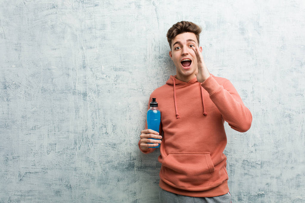 Young sport man holding an energy drink shouting excited to front. - Photo, Image