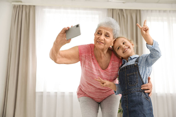 Cute girl and her grandmother taking selfie  at home - Fotó, kép