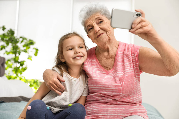 Cute girl and her grandmother taking selfie  at home - Fotografie, Obrázek