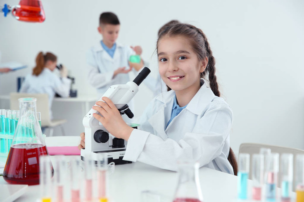 Schoolgirl with microscope at table in chemistry class - Фото, изображение