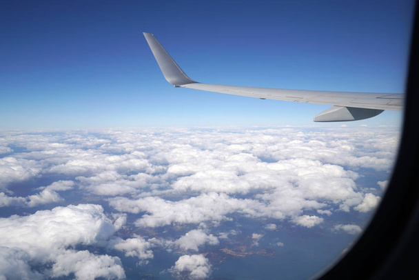Aile d'un avion volant au-dessus des nuages, par la fenêtre de l'avion
                               - Photo, image