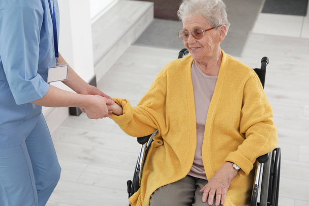 Nurse assisting senior woman in wheelchair at hospital - Fotó, kép