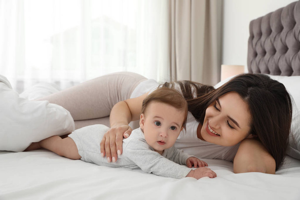 Portrait of mother with her cute baby lying on bed indoors - Foto, Bild