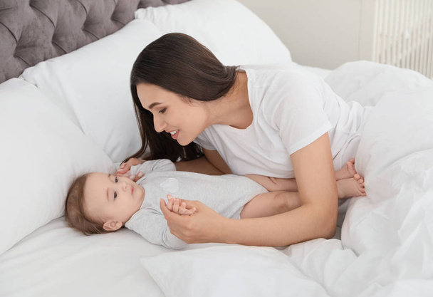 Portrait of mother with her cute baby lying on bed indoors - Photo, image