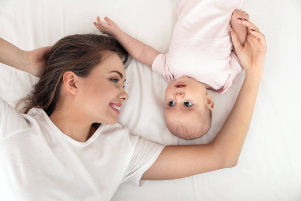 Portrait of mother with her cute baby lying on bed, top view - Foto, Imagem