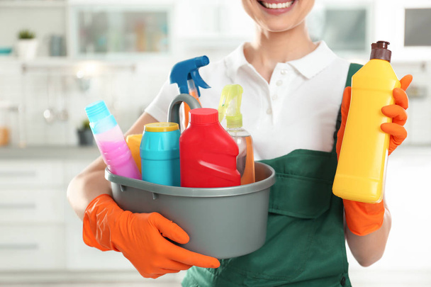 Woman with basin of detergents and bottle in kitchen, closeup. Cleaning service - Photo, Image