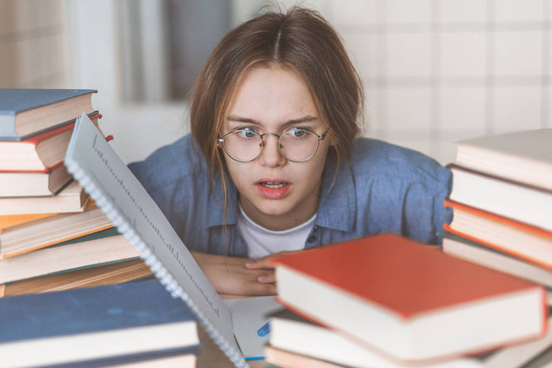 Zdenerwowana kobieta siedzi z zamkniętymi oczami wśród podręczników i laptopa, trzymając głowę w rękach, zirytowany nauką, uczucie zmęczenia i rozpaczy, przygotowanie do egzaminu, pisanie dyplomu lub zajęć - Zdjęcie, obraz