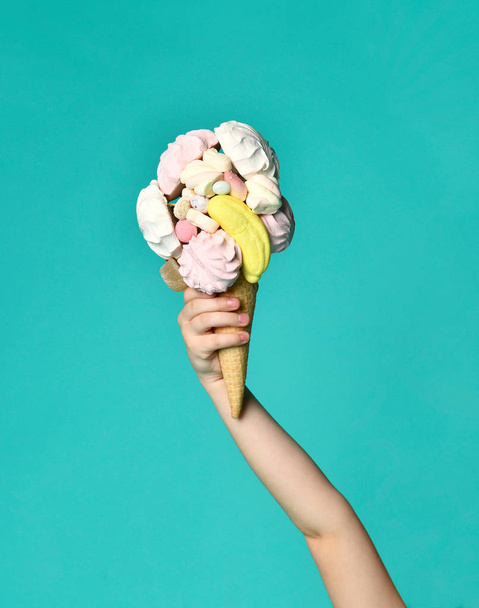 Baby girl kid hand holding big ice cream in waffles cone with tasty raspberry marshmallow marmalade on blue mint - Fotó, kép
