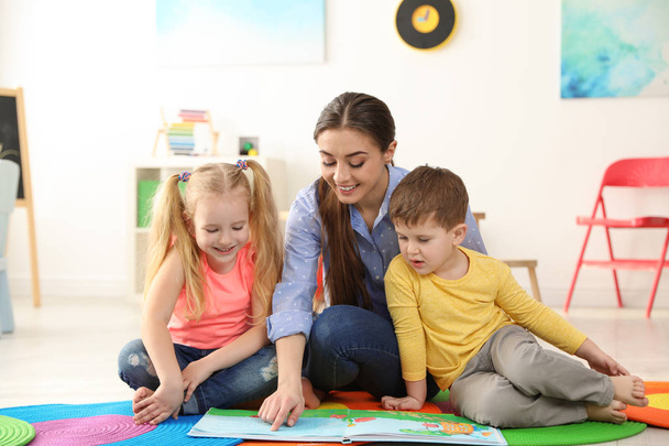 Kindergarten teacher reading book to children indoors. Learning and playing - Φωτογραφία, εικόνα