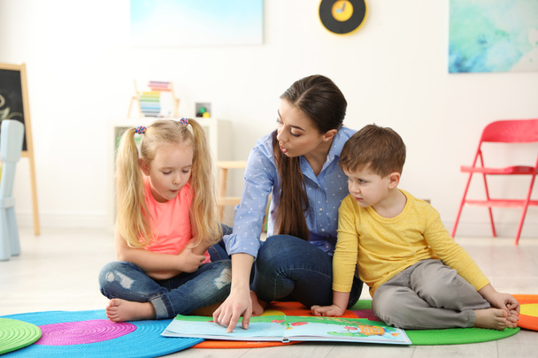 Kindergarten teacher reading book to children indoors. Learning and playing - Foto, Imagen