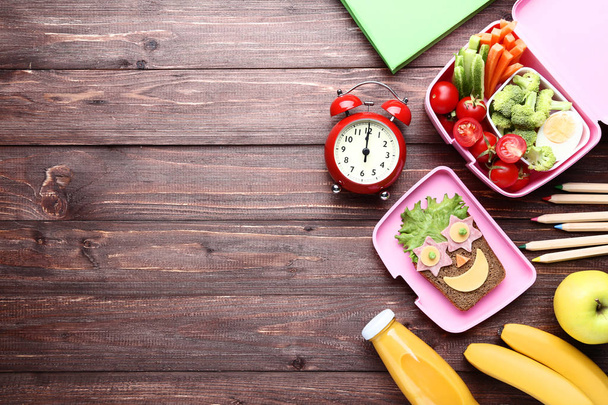 School lunch box with vegetables and alarm clock on brown wooden - 写真・画像