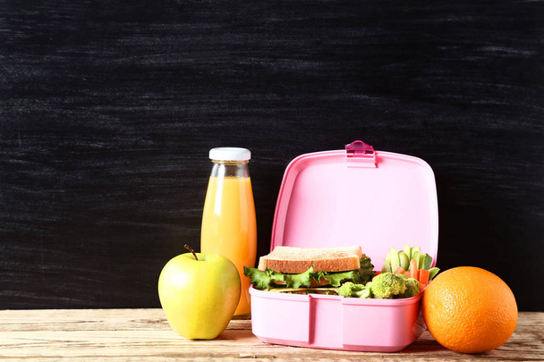 School lunch box with sandwich and bottle of juice on blackboard - Foto, imagen