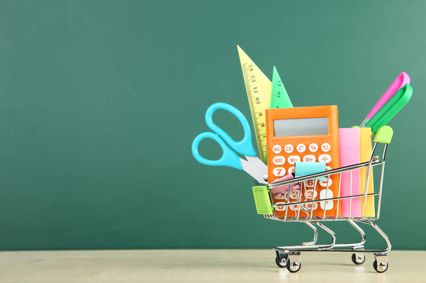 School supplies in shopping cart on chalkboard background - Foto, afbeelding