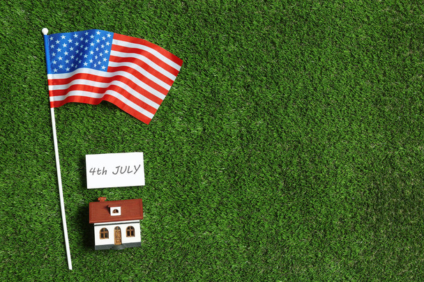 Flat lay composition with house model, USA flag and card on green grass, space for text. Happy Independence Day - Photo, Image